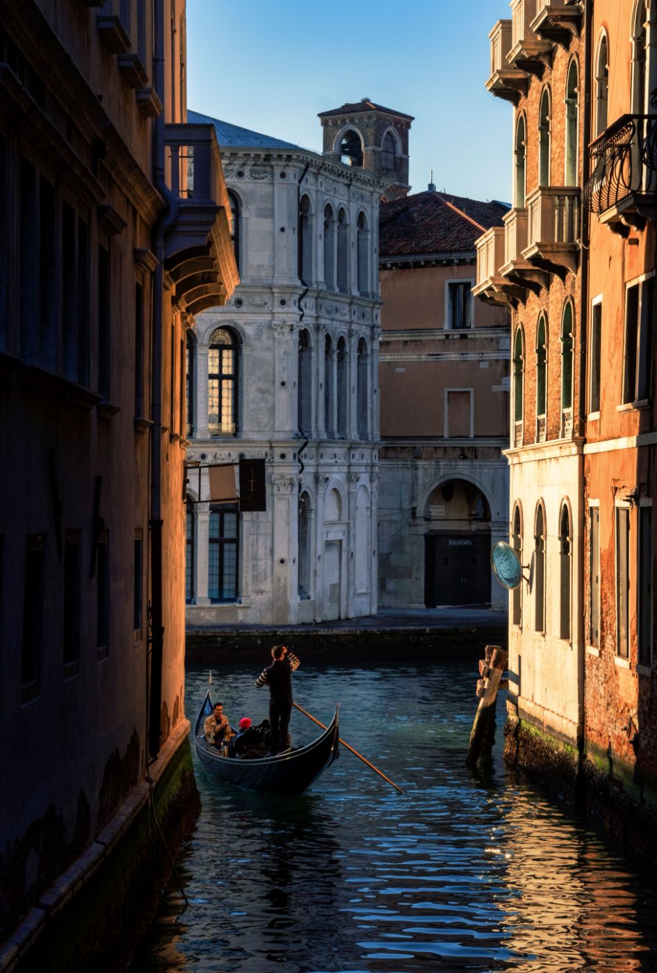 A gondola gliding down a quiet Venetian side canal at golden hour, palazzo facades glowing on either side