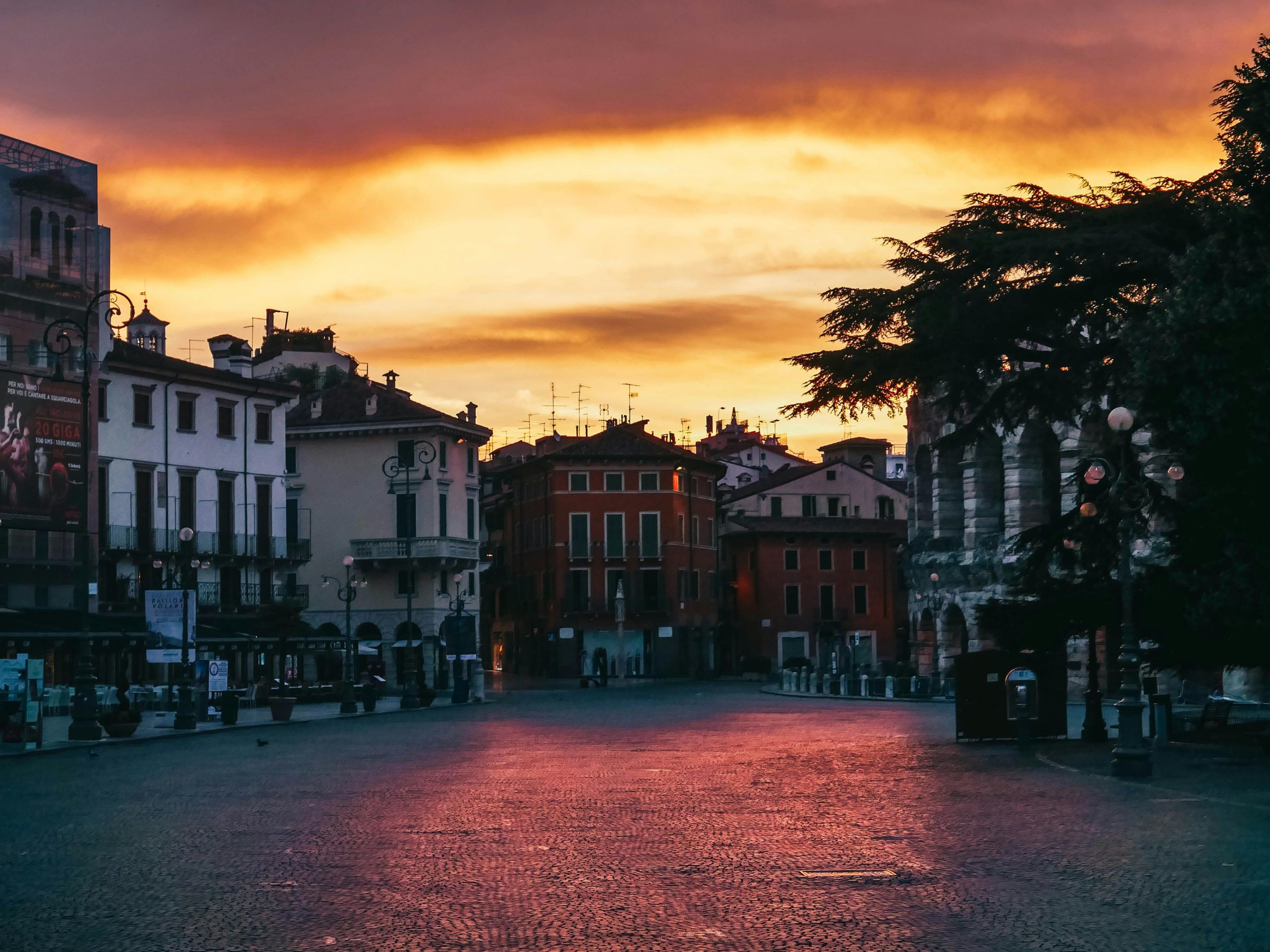 Piazza Bra in Verona at dusk — the Arena and empty cobblestones glowing under a fiery sunset sky